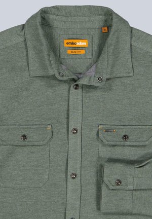 Grünes Slim-Fit-Hemd aus strukturiertem Stoff. Verfügt über zwei knöpfbare Brusttaschen mit orangefarbenen Akzenten und schwarzen Druckknöpfen auf der Vorderseite.