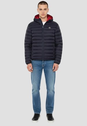 Mørkeblå dunjakke med rød indvendig foring, lynlås, hætte og to sidelommer, kombineret med blå jeans og sorte sneakers.