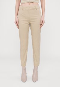 Béžové kalhoty na míru s hladkou texturou, s plochým předním dílem, postranními kapsami a střihem do kotníků, spojené s světle zbarvenými botami na podpatku.