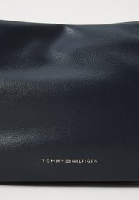 Tamsiai mėlyna, tekstūruota odinė rankinė su lengvais raukšlėmis. Apačioje yra auksinis išspaudintas "TOMMY HILFIGER" logotipas.