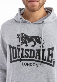Gray hoodie made of cotton blend, featuring a black lion graphic and "LONSDALE LONDON" text. Drawstrings with black ends complete the design.