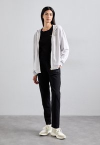 Fato de capuz cinza claro com um ligeiro brilho, usado sobre uma blusa preta, combinado com calças pretas justas e sapatilhas off-white.
