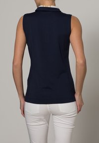 Hihaton laivastonsininen poolopaita, jossa on valkoinen kaulus, istuva malli ja sileä kangas. Takakuvassa näkyy siistit linjat ilman koristeita.