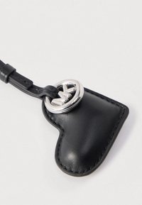 Črni usnjeni obesek za ključe v obliki srca s srebrnim kovinskim okrasjem in detajli šivanja. Vsebuje zanko za pritrditev. Gladek otip.