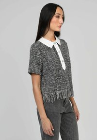 Crop top noir et blanc avec des manches courtes, un col blanc, des boutons à l'avant et un ourlet effiloché. Porté avec un pantalon taille haute gris.