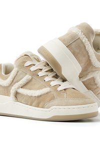 Beige Wildleder-Sneaker mit weichen Lammfell-Akzenten, weißen Schnürsenkeln und strukturiertem Gummiprofil. Mit Logo an der Seite und hinten.