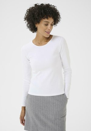 White long-sleeve top with a round neckline and a ribbed texture, paired with a gray pinstriped skirt. The fabric appears soft and comfortable.