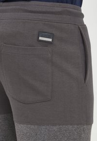 Pantalones de chándal grises con un acabado texturizado, cinturilla elástica, bolsillos laterales y un pequeño parche de marca en la parte trasera.