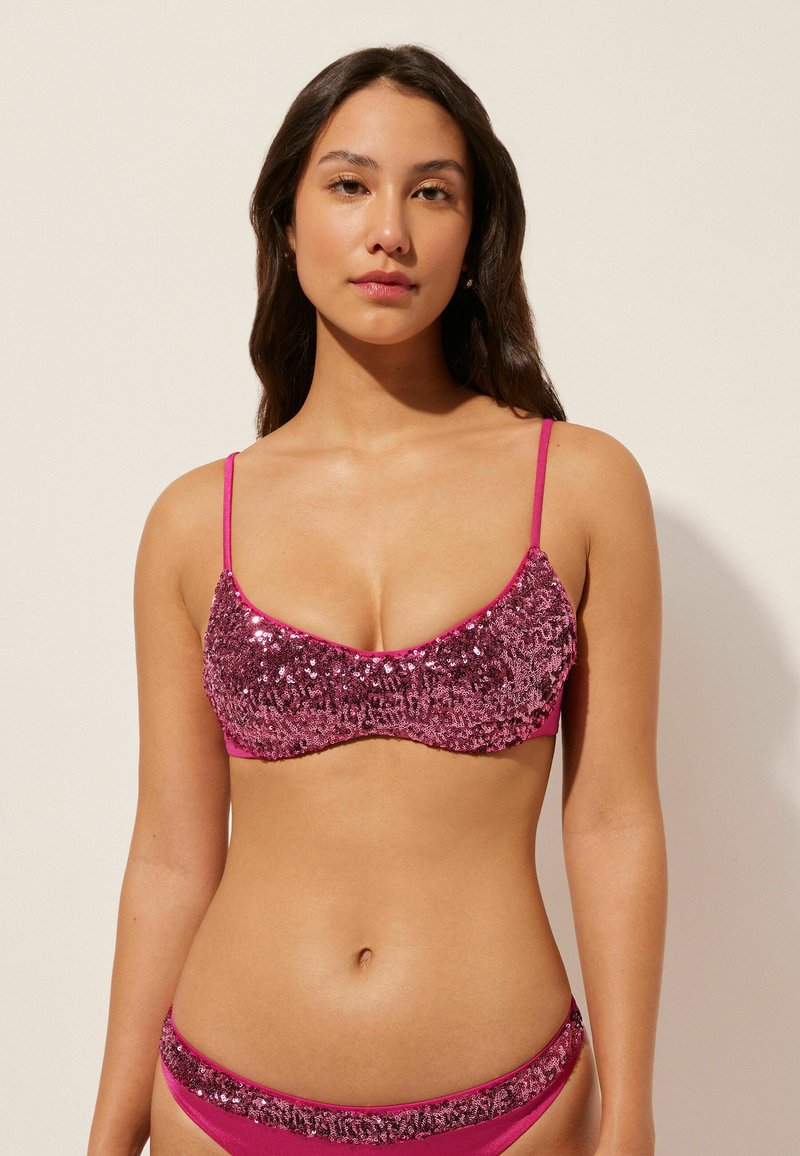 Paljettprydd rosa bikiniöverdel med tunna justerbara axelremmar och matchande botten, med en texturerad yta och slät tyg.