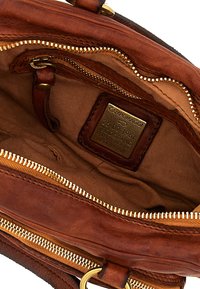 Interno di una borsa a tracolla in pelle marrone con cerniera dorata, rivestimento in tessuto e etichetta del produttore. Presenta un compartimento principale e una tasca aggiuntiva.