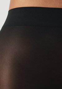 Leggings noirs à côtes avec une large taille lisse. Le tissu est transparent et légèrement texturé, mettant en valeur une vue en gros plan du matériau.