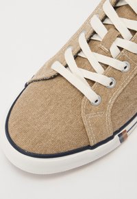Világosbarna vászon sneaker texturált felülettel, fehér fűzőkkel és fehér gumitalppal, amelynek szélein navy kék akcentus díszíti.