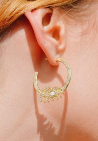 Boucle d'oreille en or avec une finition texturée, présentant un design en forme de feuille orné de strass étincelants et d'un accent en perle centrale.