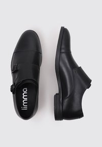 Zapatos de cuero negro con textura suave, punta redondeada, doble correa con hebilla y tacón bajo y duradero. Logo de la marca visible en el interior.