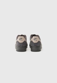 Gray suede sneakers with a black rubber sole, featuring a tan leather heel accent and Nike Air logo on the back. Rounded toe design.