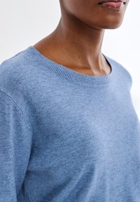 Jasnoniebieski sweter z dzianiny z okrągłym dekoltem i prążkowanymi mankietami. Tkanina wydaje się miękka i lekko teksturowana.