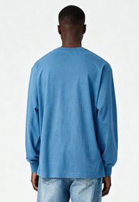 T-shirt bleu à manches longues en coton, avec un col rond et une coupe décontractée. Design simple sans motifs ni accents visibles.