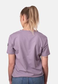 Camiseta de algodón lila con mangas cortas y un corte relajado. Presenta un cuello redondo y un pequeño parche con el logo en la manga izquierda.