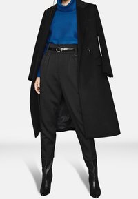 Cappotto nero su misura, maglione blu a collo alto con texture, pantaloni neri a vita alta e stivaletti neri a punta. Design elegante e schema di colori classico.