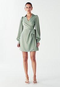 Zavinovacia šaty z jemne zelenej látky, s golierom, balónovými dlhými rukávmi, opaskom v páse a mierne rozšírenou sukňou s jemným leskom.