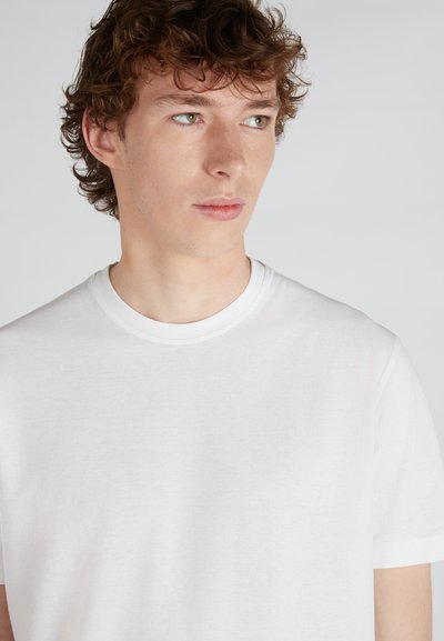 T-shirt bianco in cotone con scollatura rotonda e maniche corte, texture liscia e taglio aderente. Design minimalista senza motivi visibili.