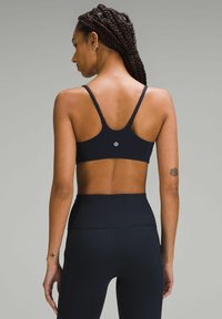 Čierny športový podprsenka s tenkými popruhmi, priliehavý dizajn, hladký povrch a logo na strede chrbta. Spárované s vyhovujúcimi legínami s vysokým pásom.