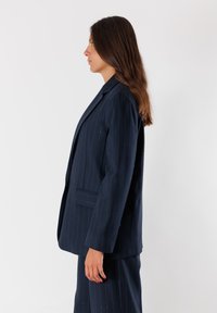 Blazer a righe navy con un design strutturato, chiusura a un bottone e due tasche frontali. Tessuto liscio con una finitura professionale.