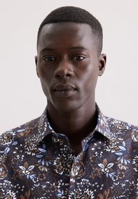 Camicia a maniche corte con motivo floreale in marrone, bianco e blu su uno sfondo scuro; realizzata in cotone con un design di colletto normale.