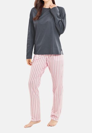 Person wearing long-sleeve dark gray shirt and light pink striped pajama pants, standing barefoot against plain background.