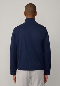 Chaqueta azul marino con cuello alto, mangas largas y puños abotonados. Presenta una textura suave y un corte recto con dos botones en el dobladillo.