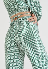 Grön och vit mönstrad klädsel med en åtsittande topp med knytdetalj och hög midja, löst sittande byxor med blommotiv.