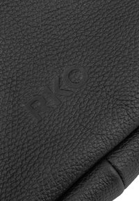 Surface en cuir noir texturé avec le nom de marque "RAYO" en relief subtil sur le matériau plié.