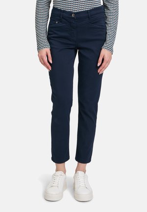 Pantaloni blu navy con vestibilità slim, dotati di tasche frontali e vita a media altezza, abbinati a sneakers bianche per un contrasto.