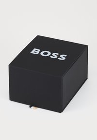 Must värviline must ristkülikukujuline karp mati pinna ja peal prinditud sõna "BOSS" paksu hõbedase fondiga. Väike silt eristuvates värvitoonides.