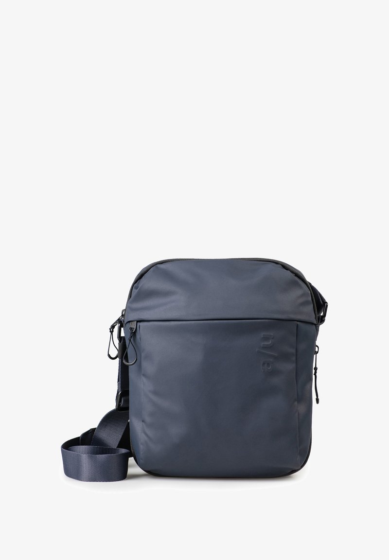 Kompakte navyblaue Umhängetasche mit verstellbarem Riemen, vordertasche mit Reißverschluss und dezent geprägt Logo auf der Vorderseite.