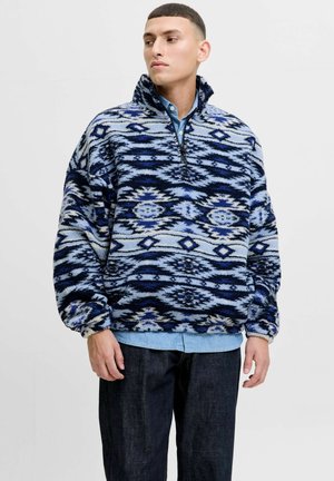 Blauw en zwart gestepte fleece pullover met hoge kraag, halve rits en elastische manchetten; gedragen over een lichtblauw spijkerhemd.
