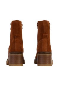 Stivaletti in suede marrone alla caviglia con punta rotonda, chiusura con zip e tacco in legno impilato, caratterizzati da cuciture dettagliate lungo il bordo della suola.