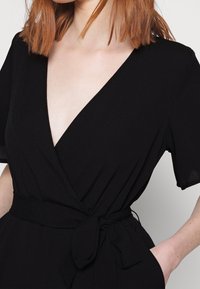 Mono cruzado negro con mangas cortas, escote en V profundo y cintura anudada. Hecho de tela suave con un ajuste favorecedor.