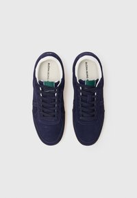 Adidași din suede navy cu tălpi albe, cu vârf rotund, design cu șireturi și o etichetă verde pe limbă. Suprafață texturată cu detalii de cusătură.