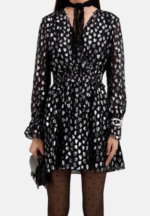 Robe noire à manches longues ornée de motifs cœurs argentés, manches transparentes, taille élastique, accompagnée de collants noirs à pois et d'une pochette noire.