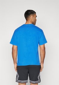 Camiseta de algodón azul con cuello redondo y mangas cortas, detalles de costura visibles, combinada con pantalones cortos de malla negra con acentos blancos.