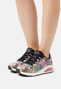 Mehrfarbige Sneakers mit einem schwarzen Mesh-Obermaterial, das über Cartoon-Grafiken verfügt, schwarzen Schnürsenkeln und einer weißen Zwischensohle mit einem pinken Luftpolster-Detail.