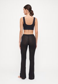 Schwarzer Sport-BH mit breiten Trägern und Rundschnitt auf der Rückseite, kombiniert mit durchsichtigen schwarzen Schlagleggings mit seitlichen Schlitzen am Saum.