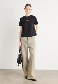 Svart bomulls T-skjorte med rød "Calvin Klein" logo, kombinert med lyse denim bukser med bred ben og en liten svart håndveske.