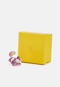 Klar kristallfigur av en katt med lila och rosa accenter, bredvid en texturerad gul presentlåda.