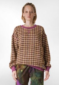 Pulover tricotat într-un model în carouri maro, roz și verde. Are un guler și manșete purpurii, cu un tiv rotund și un detaliu logo de accent.