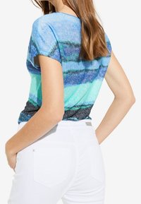 Top de manga corta a rayas azul y verde, hecho de una tela suave, combinado con jeans blancos de cintura alta que presentan un diseño de bolsillo sencillo.