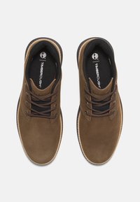 Brown suede shoes with a round toe, dark brown laces, a black inner lining, and a beige rubber sole. Features "Timberland" branding.