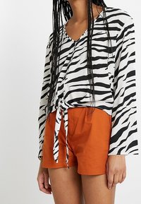 Blusa a maniche lunghe con stampa zebra bianco e nero, con un nodino frontale, abbinata a pantaloni corti arancioni. Tessuto dal tocco morbido, vestibilità rilassata.
