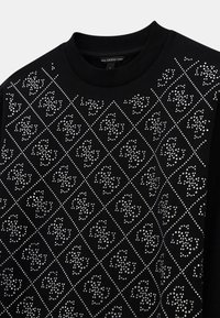 Sweat-shirt noir avec un motif en diamant créé avec des clous en argent, mettant en valeur une surface texturée et un col rond.